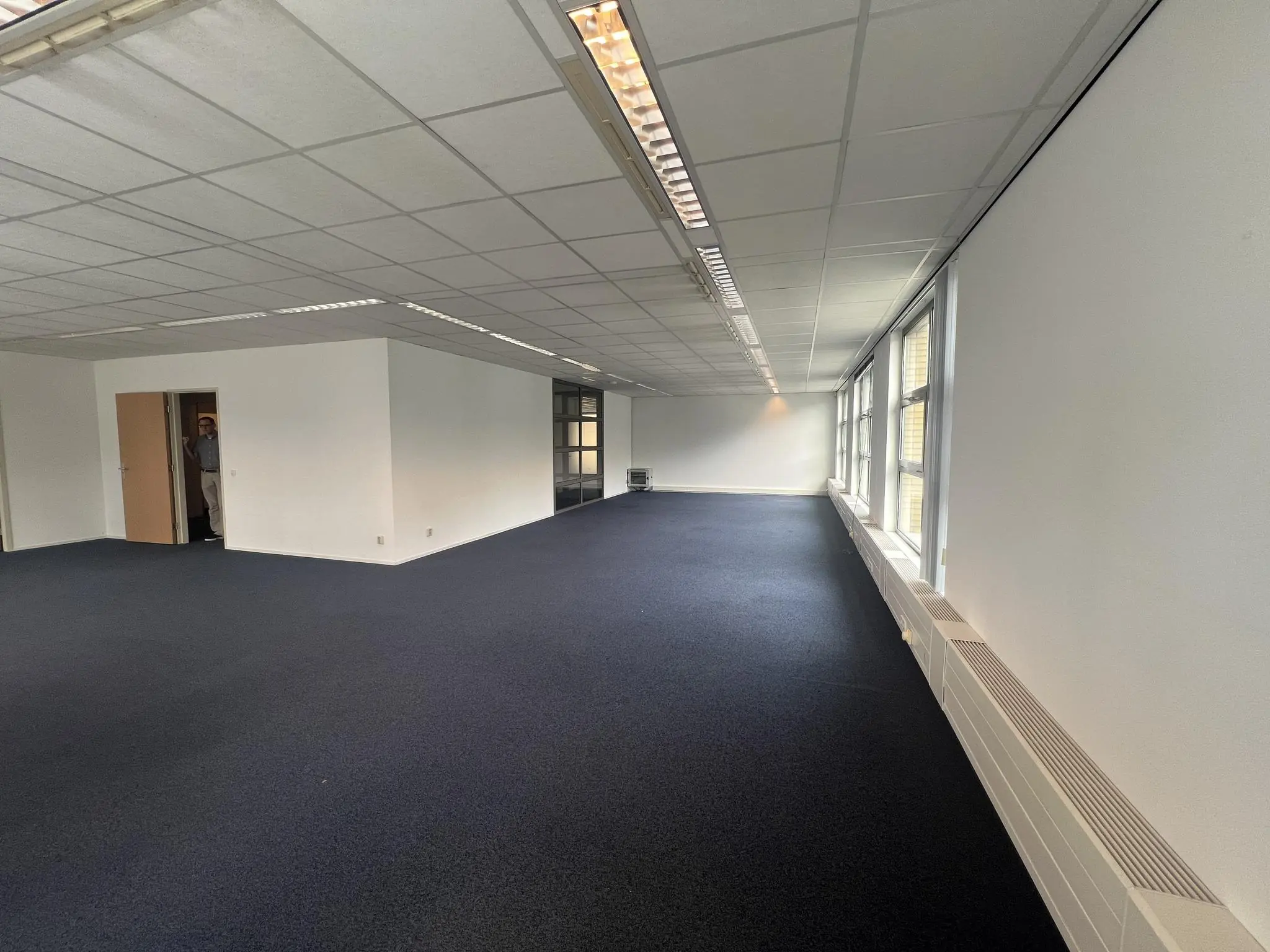 Lege kantoorruimte aan de Rivium 2e Straat met donker tapijt, systeemplafond en grote ramen aan de rechterkant.